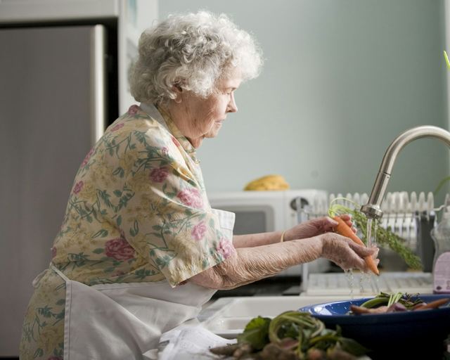Een oudere vrouw spoelt wortelen in haar keuken