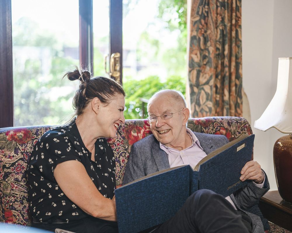 Een vrouw en een oudere man bekijken samen een fotoalbum in de zetel